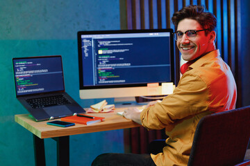 Side back view smiling young full-stack developer software engineer IT specialist programmer man in shirt work at home writing code on laptop pc computer checking database Program development concept
