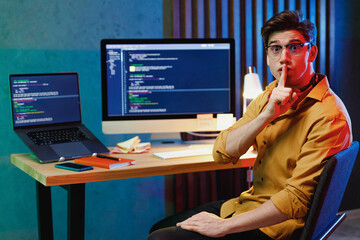 Young secret software engineer IT specialist programmer man wear shirt work at home writing code on laptop pc computer say hush be quiet with finger on lips shhh gesture. Program development concept