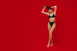 © ViDi Studio - Full body young sexy caucasian smiling hot happy slender woman 20s with perfect fit body wear black underwear hold hair isolated on plain red background studio portrait. People female beauty concept.