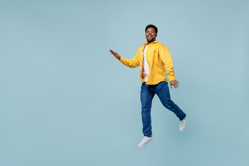 Wall Mural - Full body side view young man of African American ethnicity 20s wear yellow shirt jump high walking going run isolated on plain pastel light blue background studio portrait. People lifestyle concept.