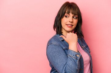 Young caucasian woman isolated on pink background points with thumb finger away, laughing and carefree.