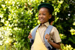 Smiling african american scout girl in uniform with backpack looking away against plants