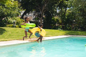 Wall Mural - African american siblings jumping with inflatable ring in swimming pool on sunny day