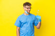 © luismolinero - Dentist blonde man holding tools isolated on background looking to the side and smiling