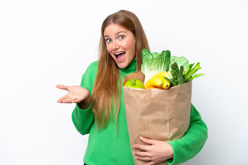 Young caucasian woman holding a grocery shopping bag isolated on white background with shocked facial expression