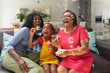 © WavebreakMediaMicro - Cheerful african american girl blowing bubbles with mother and grandmother at home