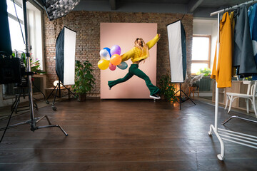 Wall Mural - Fashion studio portrait of a happy young woman with balloons jumping, backstage of photoshooting .
