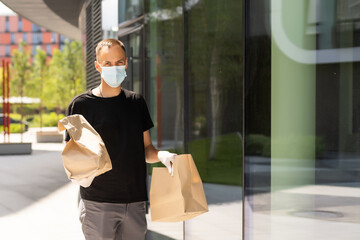 Wall Mural - Delivery guy with protective mask and gloves holding bag with groceries in front of a building.