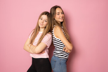 Wall Mural - Portrait of two cheerful young women standing together and looking at camera isolated over pink background