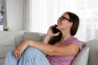 © Evrymmnt - Portrait of young brunette woman wearing eyeglasses talking on the phone and smiling. Joyful female sitting on the couch at home having fun phone call. Background, copy space, close up