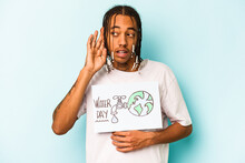 Young African American Man Holding Protect Our Planet Placard Isolated On Blue Background Trying To Listening A Gossip.