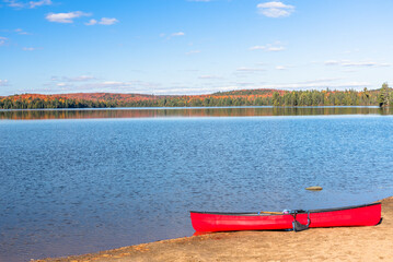 Wall Mural - Empty red canoe on a sandy beach on a beutiful lake with forested shores on a clear autumn day