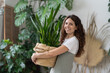 © DimaBerlin - Love for plants. Joyful caucasian woman hold pot with green houseplant happy smiling. Positive florist create indoor garden with house flowers at home. Freelancer gardener small business owner girl