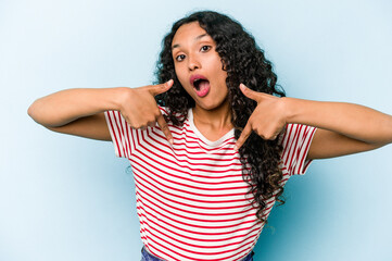 Wall Mural - Young hispanic woman isolated on blue background points down with fingers, positive feeling.