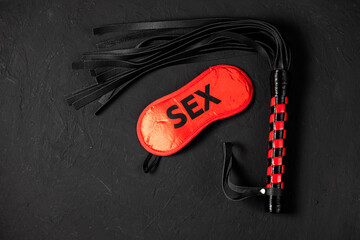 BDSM, bondage play, fetish wear and kinky sex toy concept with close up on erotic mask and red handcuffs isolated on black silk background