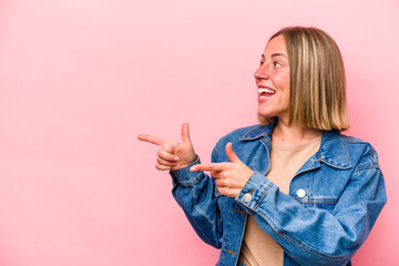 Wall Mural - Young caucasian woman isolated on pink background points with thumb finger away, laughing and carefree.