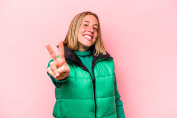 Wall Mural - Young caucasian woman isolated on pink background joyful and carefree showing a peace symbol with fingers.