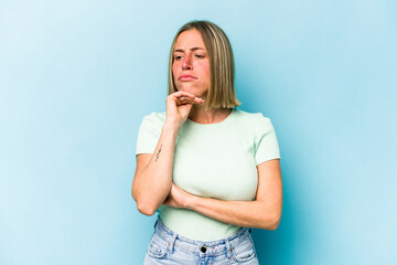 Wall Mural - Young caucasian woman isolated on blue background suspicious, uncertain, examining you.