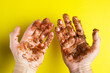 Hands smeared with melted chocolate on a yellow background. Hands in shit.