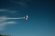© Екатерина Бучинская - A small plane maneuvers in a blue sky with a contrail. High quality photo
