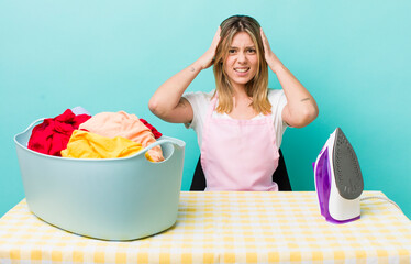 pretty blonde woman feeling stressed, anxious or scared, with hands on head. iron and clothes concept