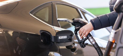 Female worker hand holding nozzle fuel fill oil into car tank at a pump gas station, For the concept transportation power business technology concept