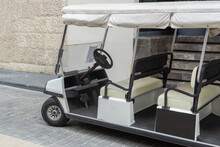 Golf Car On The Sidewalk. An Empty Tourist Shuttle Is Parked Outside The Hotel. Electric Golf Cart