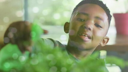 Poster - Animation of lights on water over happy african american boy watering houseplants