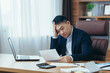 © Liubomir - Young asian male accountant, office worker working with documents, tired, sitting at desk in office