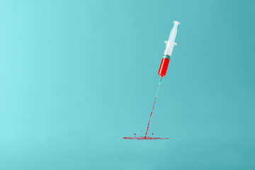 Creative concept of vaccination on a blue background. Medical syringe spewing red liquid with splatter.