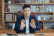 © Liubomir - Asian man diplomat, director, businessman looking at the camera smiling, concluding a contract, holding a meeting, video call conference, consults. Explains, sits at a table in the office at work