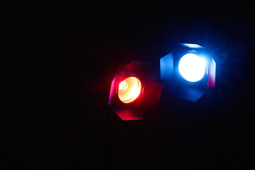 Bright blue and red spotlights near brick wall in dark room, space for text