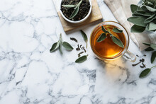 Cup Of Aromatic Sage Tea, Dry And Fresh Leaves On White Marble Table, Flat Lay. Space For Text