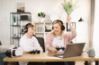 © sofiko14 - Mother with son sitting together at the table and playing video games with joysticks. Mom raised her hands up and screaming while winning the game. Woman helps to play her son.