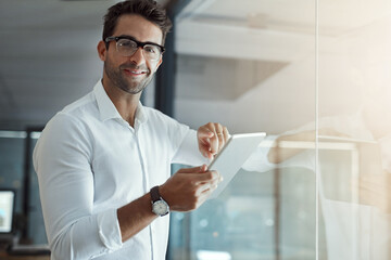 Wall Mural - Im on the job. Cropped portrait of a handsome young businessman working on his digital tablet while standing in the office.