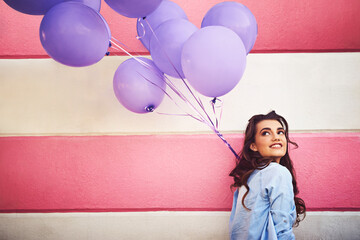 Poster - Having colourful fun in the city. Cropped shot of a beautiful young woman holding purple balloons against a wall outside.