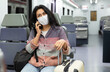 Young adult woman passenger wearing face mask for disease protection sitting in intercity train and using mobile phone