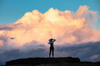 © Austockphoto - Woman standing with hands on head on rock against a dramatic cloud backdrop