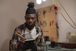 © Wavebreak Media - African american young craftsman with dreadlocks writing in book while working in leather workshop