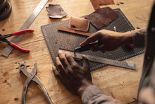 Cropped Hands Of African American Young Craftsman Cutting Leather On Layer Cutting Mat At Workbench