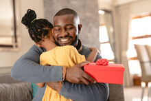 Happy African American Father Hugging Daughter After Receiving Red Present From Her At Home