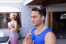 Young Biracial Man Practicing Yoga By Woman At Patio In Backyard
