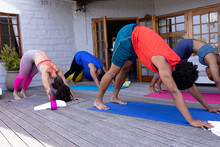 Young Multiracial Friends Practicing Downward Facing Dog Pose Together On Patio At Backyard