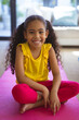 © Wavebreak Media - Full length portrait of smiling biracial girl sitting on pink yoga mat in living room at home