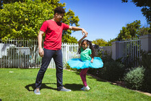 Full Length Of Multiracial Father Spinning Daughter In Backyard Garden On Sunny Day