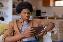 African American Young Man Using Digital Tablet While Sitting On Sofa At Home