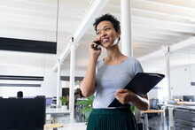 Smiling Biracial Businesswoman Talking On Smart Phone In Creative Office