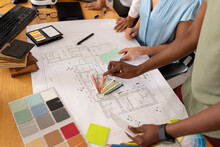 Female Architects With Blueprint Discussing Over Color Swatch In Meeting At Office