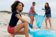 © Wavebreak Media - Smiling young woman with multiracial female friends collecting plastic waste at beach