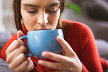 Close-up Of Young Biracial Woman Drinking Coffee In Blue Mug At Home